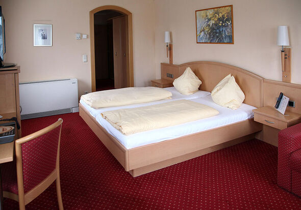 Eines von Zwei Betten, hier das Doppelbett mit Fernseher und einem kleinen Tisch im selben Raum, dahinter der Eingang in den Flur